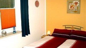 Een slaapkamer met een bed, een raam met jaloezieën, een nachtkastje, een lamp en een decoratie aan de muur.