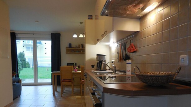 Een moderne keuken met een groot eiland, een eethoek met een tafel en stoelen, en een uitzicht op een groen buitengebied door een glazen deur.