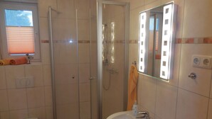 Een badkamer met toilet, douchecabine, wastafel en spiegel.