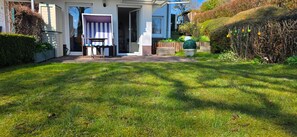 Une maison avec un jardin devant, une chaise de plage à rayures et une petite table.