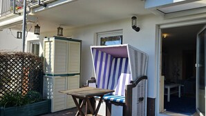 Un balcone con una sedia a righe, un tavolino e un recinto in pannelli intrecciati.