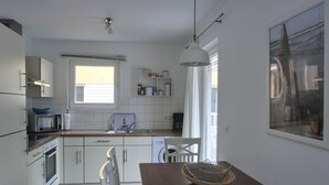 A modern kitchen with white cabinets, a wooden dining table, and a hanging light fixture.
