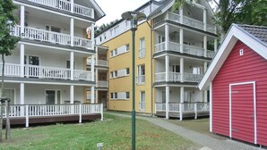 A multi-story residential building with balconies, a red garage, and a paved courtyard.