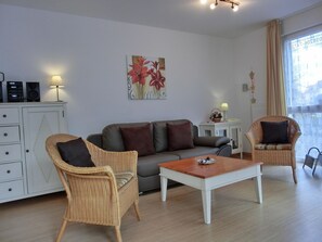 Un salon comprenant un canapé, deux fauteuils en osier, une table basse, un meuble avec des haut-parleurs et un tableau accroché au mur.