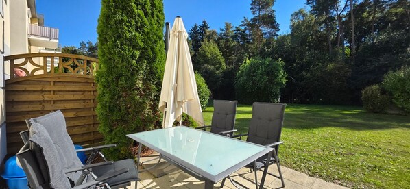An outdoor patio with a glass table and chairs, a wooden fence, and a large umbrella.