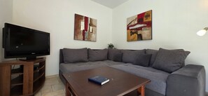 A living room with a flat-screen TV, a sectional sofa, and two abstract paintings on the wall.