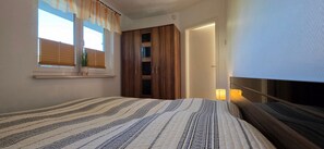 A bedroom with a bed, a window with blinds, a wardrobe, and a bedside lamp.