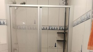 Un baño con ducha envuelta en vidrio, inodoro con una toalla naranja y paredes de azulejos.