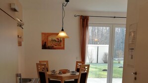 Una cocina con una mesa de comedor y sillas, un lámpara colgante y vistas al exterior a través de un puerta de vidrio.