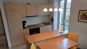 A compact kitchen with a central island, a sink, and a stove. There are two chairs and a small table. - Apartment i25 - 56 m² large 3-room apartment 3 pers. on the 1st floor in the house Lee (Graal-Müritz)