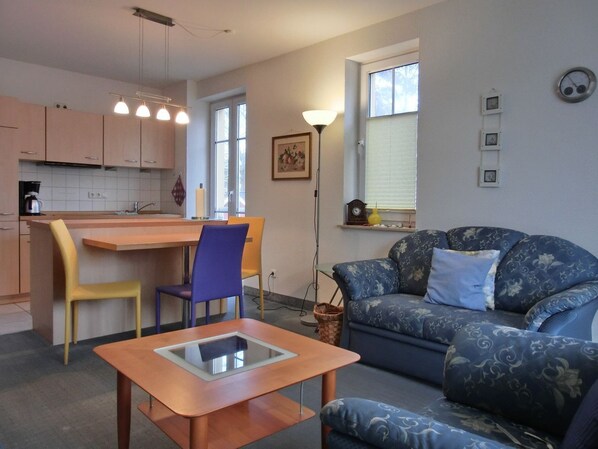 Un espace de vie compact comprenant un coin cuisine, un coin repas et un espace détente avec un canapé et une table basse.