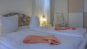 A hotel room with two beds, white linens, a floral headboard, a white chair, and a lamp. - Apartment i25 - 56 m² large 3-room apartment 3 pers. on the 1st floor in the house Lee (Graal-Müritz)