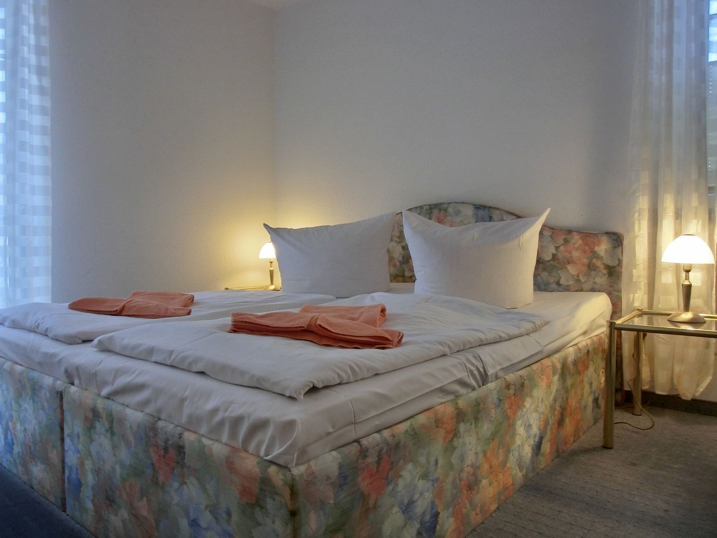 Una habitación de hotel con una cama grande, dos lámparas de noche y un cabecero floral.