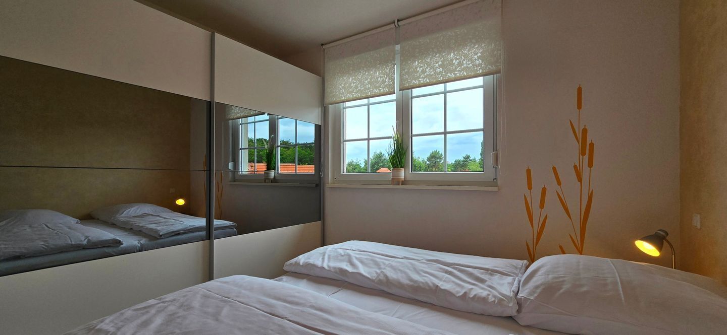 A bedroom with a bed, a window with a view, a mirror, and a wall-mounted lamp.