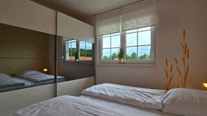 Ein Schlafzimmer mit Bett, Fenster mit Blick, Spiegel und Wandlampe.