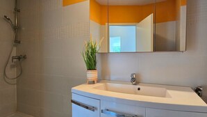 Ein modernes Badezimmer mit einem weißen Waschbecken, einem Spiegel und einer Dusche.