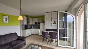 Ein modernes Wohnzimmer mit einem schwarzen Sofa, einem Glastisch und einem Essbereich mit violetten Stühlen.