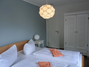 A neatly made bed with white linens and two pillows, a bedside table with a decorative item, and a hanging light fixture.
