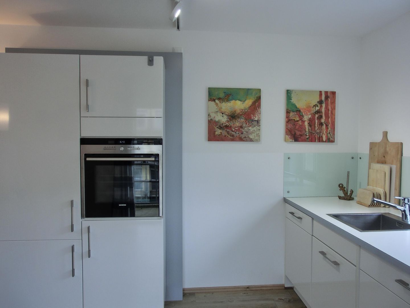 Eine moderne Küche mit weißen Schränken, einem Backofen, einer Spüle und zwei abstrakten Bildern an der Wand.