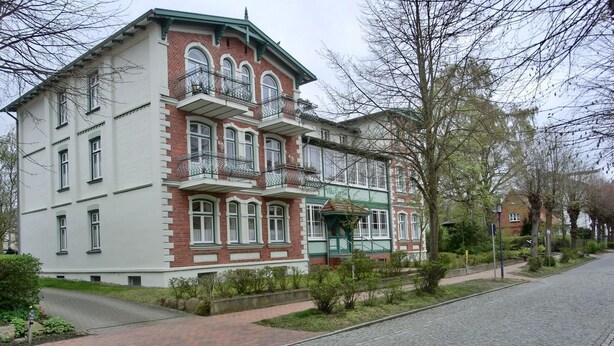 Un edificio de dos pisos con balcón, toldo verde y fachada de ladrillo.