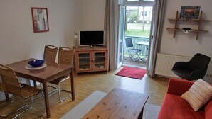Una sala de estar con una mesa de madera, un sofá rojo, un televisor y un balcón con una silla.