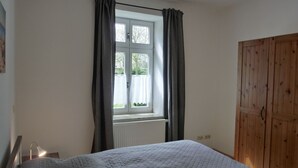 Un dormitorio con cama, ventana con cortinas, radiador y armario de madera.