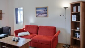 Un salón con un sofá rojo, una mesa de centro de madera, una lámpara de pie y una estantería.