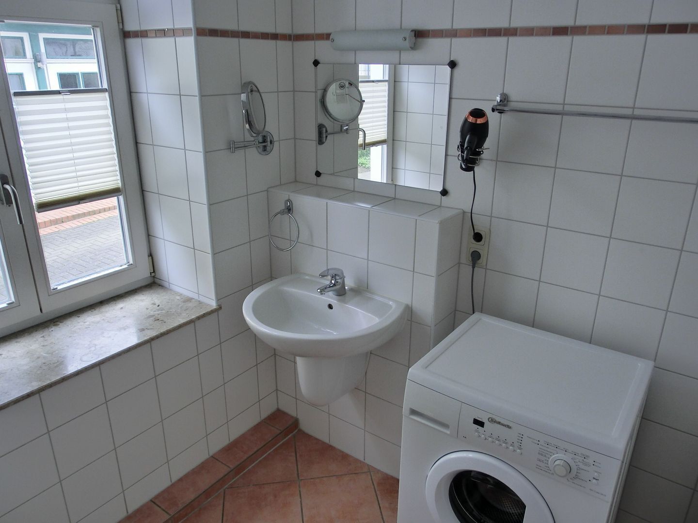 Une petite salle de bain avec un lavabo, un miroir, une fenêtre et un lave-linge.