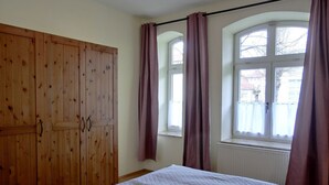 A bedroom with a bed, wooden wardrobe, and windows with curtains. - Vacation apartment LVC11 - 2-room apartment for 4 pers. with WLAN, pets allowed (Graal-Müritz)
