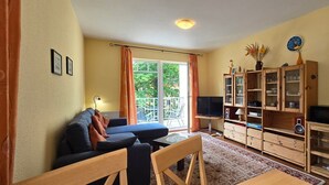 Ett vardagsrum med en soffa, ett soffbord, en tv, ett träskåp och ett fönster med gardiner.