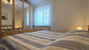 A bedroom with a large bed, a wardrobe with a mirror, a window with curtains, and a bedside lamp. - Vacation apartment P1 - 2-room apartment with terrace in the town center (Graal-Müritz)