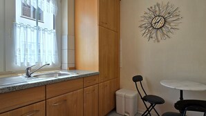 A kitchen with wooden cabinets, a granite countertop, a sink, a small round table, and a decorative wall clock. - Vacation apartment P1 - 2-room apartment with terrace in the town center (Graal-Müritz)
