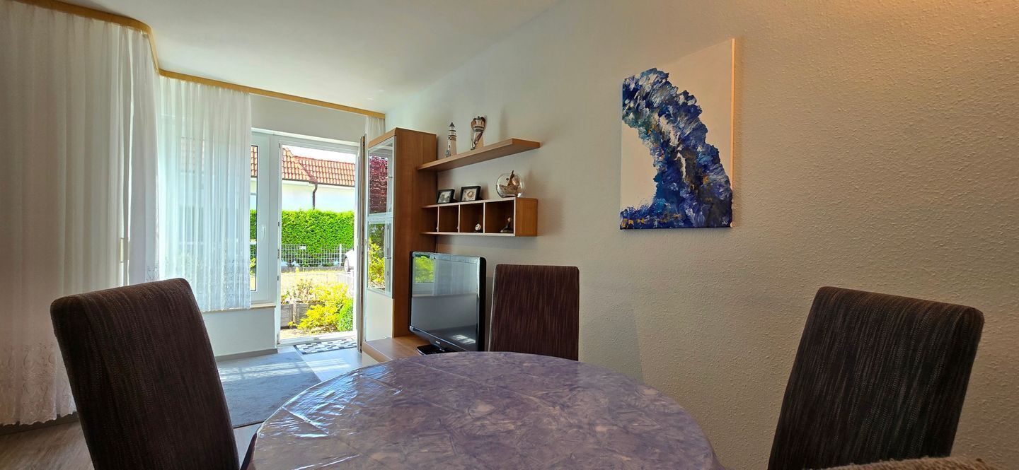 A dining area with a round table, chairs, a TV, and a shelf with decorative items.