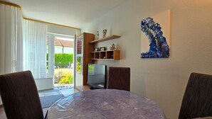 A dining area with a round table, chairs, a TV, and a shelf with decorative items. - Vacation apartment P1 - 2-room apartment with terrace in the town center (Graal-Müritz)