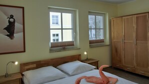 A bedroom with a wooden bed, two bedside tables with lamps, a wooden wardrobe, and two windows with blinds. - Apartment L32 - "Lütte Möw" - 2-room apartment for 4 people on the 1st floor with WiFi (Graal-Müritz)
