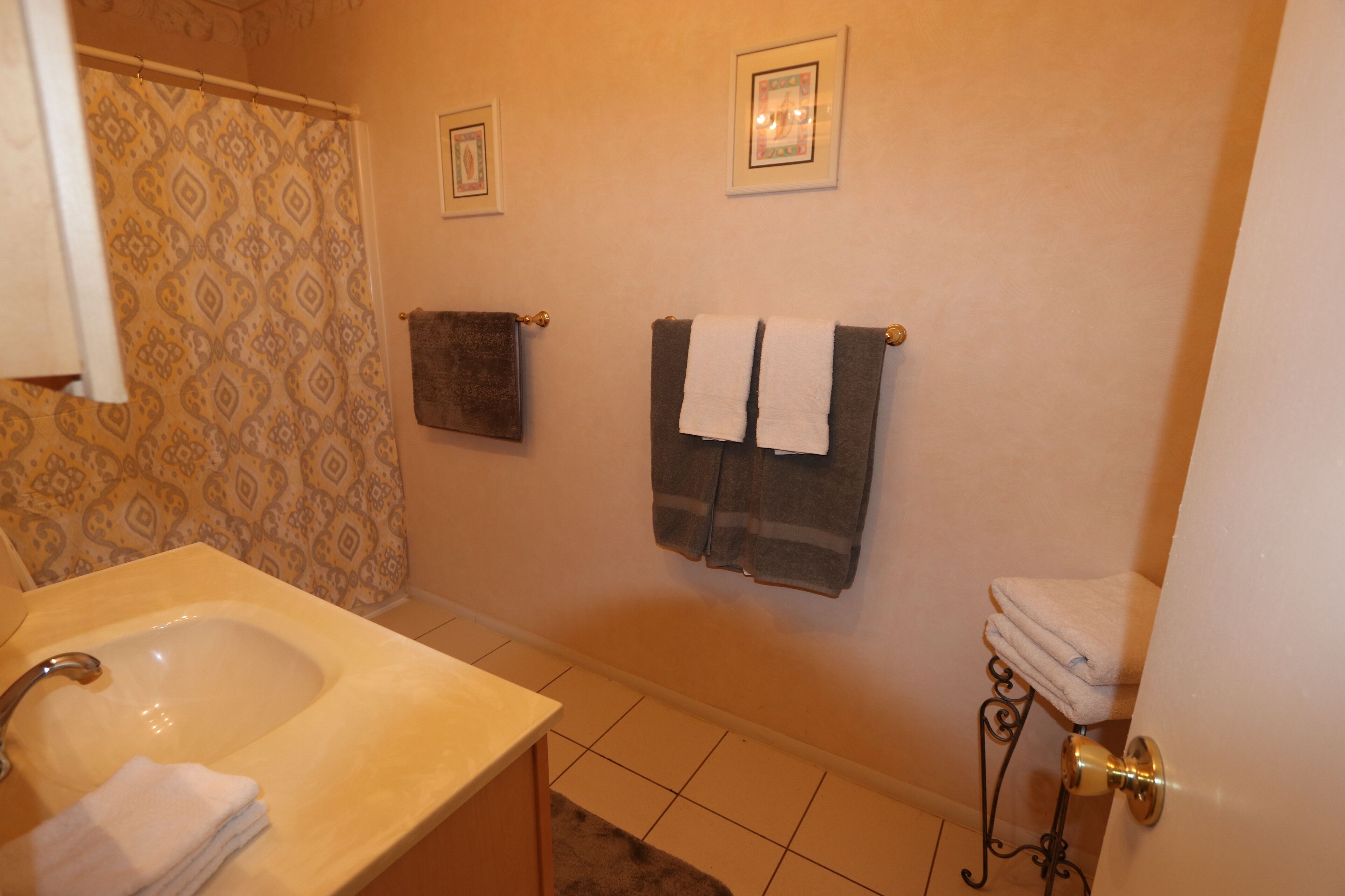 A bathroom with a sink, two towels on the wall, and a shower curtain.