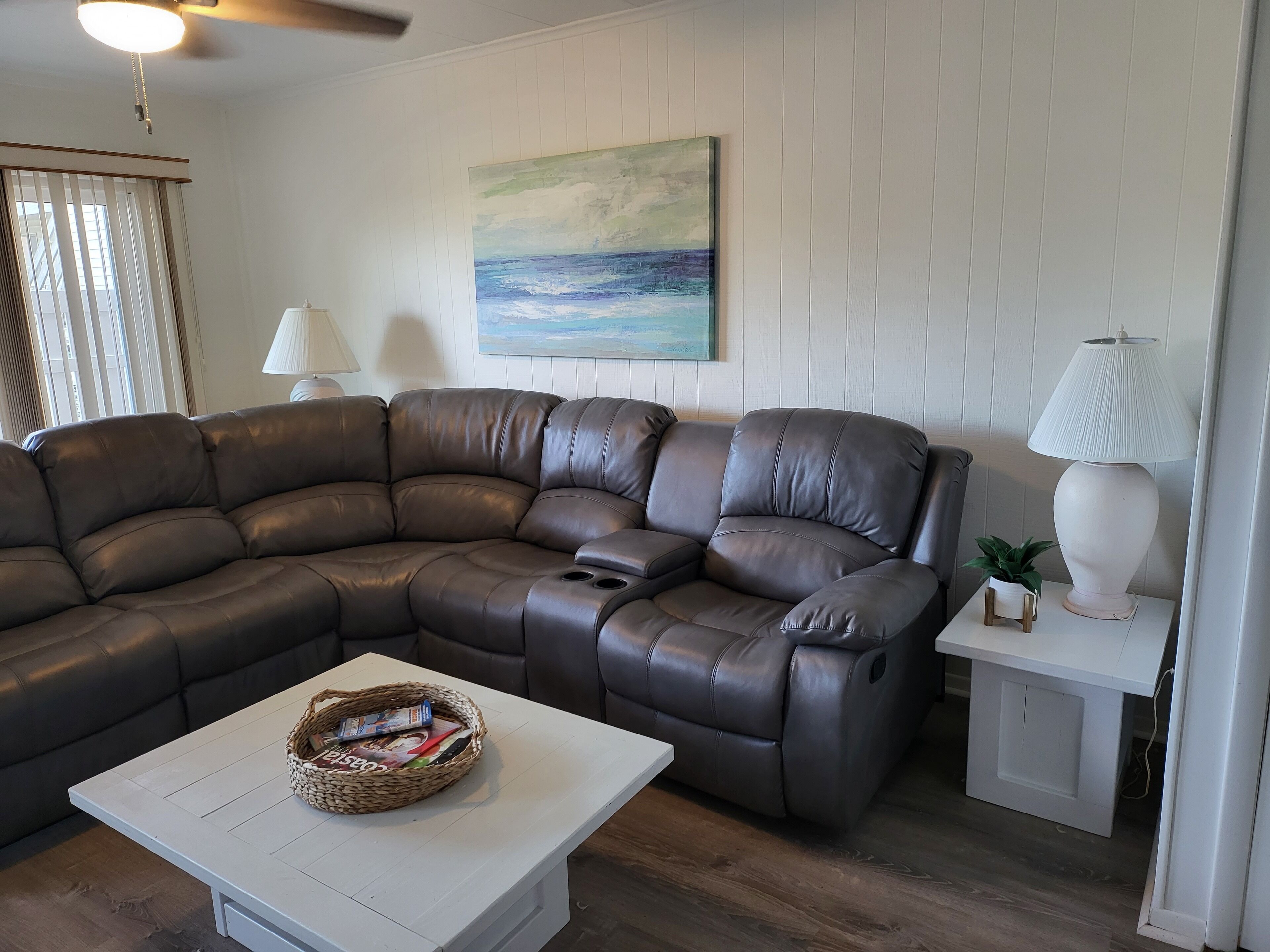 A living room with a brown leather sectional sofa, a white coffee table, and a lamp on a side table.