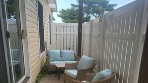 A covered patio area with a wicker sofa and a small table, a concrete step leading to a sliding glass door, and a white fence. - ABOUT 5 BLOCKS FROM THE BEACH/ OCEAN / NORTH END OF BOARDWALK (Ocean City)