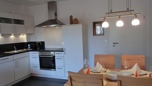 A modern kitchen with white cabinets, a stove, and a dining area with wooden chairs and a table set for two. - Vacation apartment L31- "Fürstenhof" - 2-room apartment for 4 people on the 2nd floor with WLAN (Graal-Müritz)