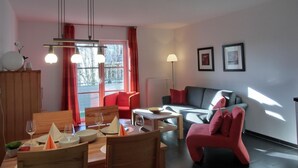 A modern living room with a dining area, a red sofa, a grey sofa, and a red armchair. There are two framed pictures on the wall and a floor lamp. - Vacation apartment L31- "Fürstenhof" - 2-room apartment for 4 people on the 2nd floor with WLAN (Graal-Müritz)