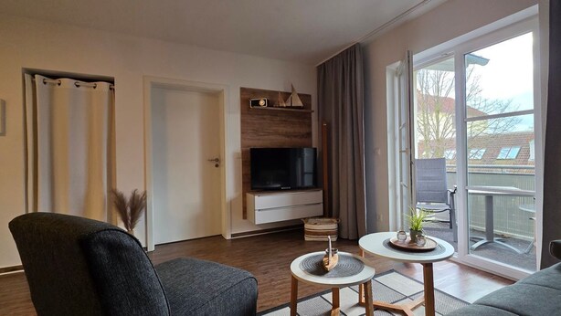 A modern living room with a flat-screen TV, a sofa, a chair, and a small table with decorative items. - Apartment L28 - 2-room apartment on the 2nd floor, approx. 45 m² for 4 persons with WLAN (Graal-Müritz)