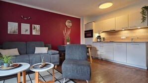 A modern living room with a grey sofa, a small round table, and a grey armchair. There is a kitchen area with white cabinets and a wooden countertop. - Apartment L28 - 2-room apartment on the 2nd floor, approx. 45 m² for 4 persons with WLAN (Graal-Müritz)