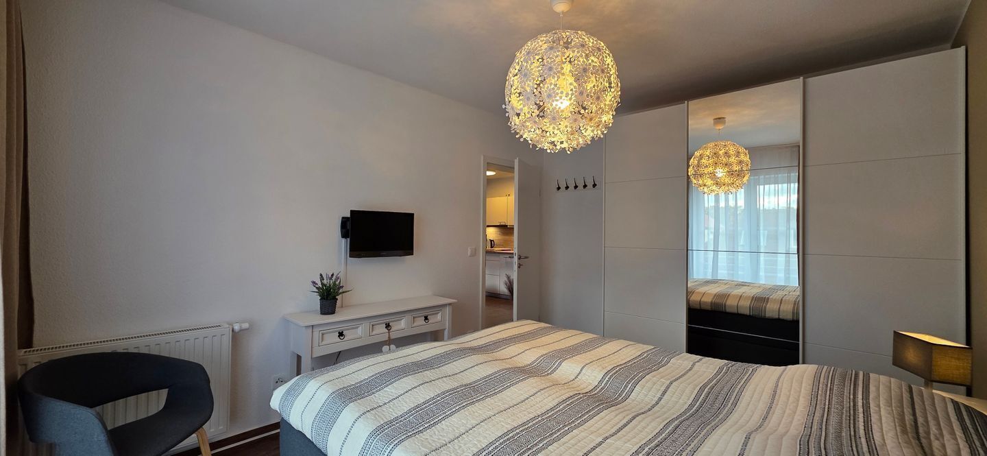 Ein modernes Schlafzimmer mit einem großen Bett, einem Fernseher, einem Schreibtisch und einem Spiegel.