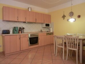 A compact kitchen with wooden cabinets, a microwave, a toaster, and a dining area with a table and chairs.