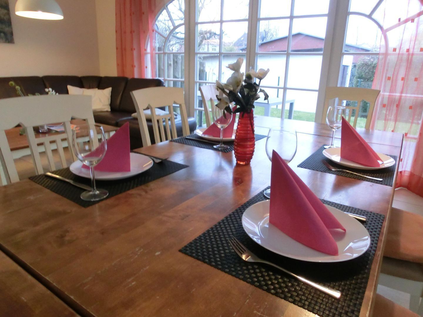 Una mesa de comedor dispuesta con servilletas rosas, platos y cubiertos, con un florero en el centro.
