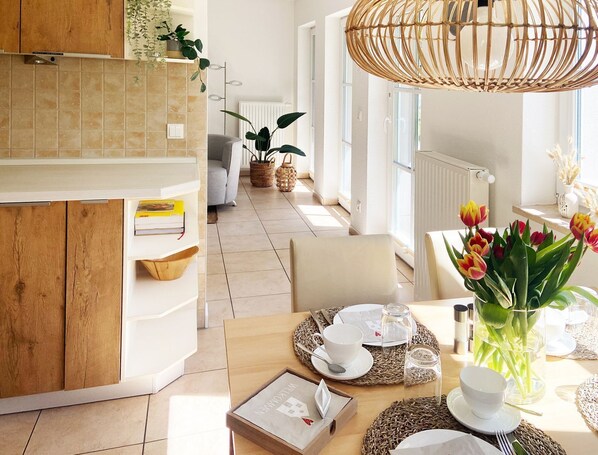 A modern kitchen with wooden cabinets, a dining area with a table set for two, and a view of the living room.