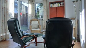 Um quarto com duas cadeiras de escritório pretas, uma cadeira de vime e uma estante de madeira.