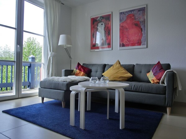 A living room with a grey sofa, two colorful pillows, a white coffee table, and two framed artworks on the wall.