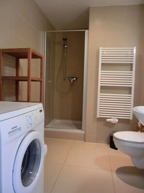A compact bathroom with a washing machine, a glass-enclosed shower, and a toilet.