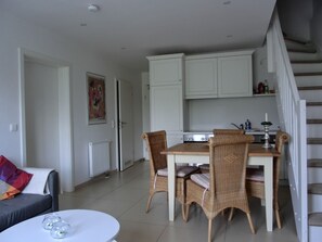 A dining area with wicker chairs, a white table, and a kitchen with white cabinets.